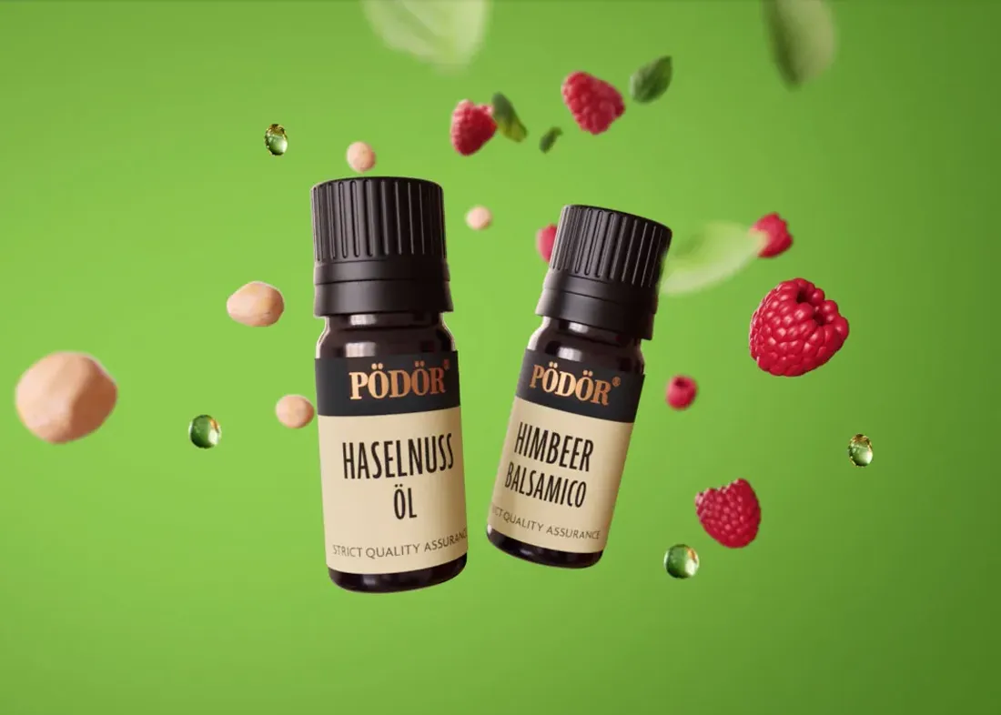 Zwei kleine Pödör Probierflaschen mit Haselnussöl und Himbeeressig zwischen frischen Haselnüssen und Himbeeren.