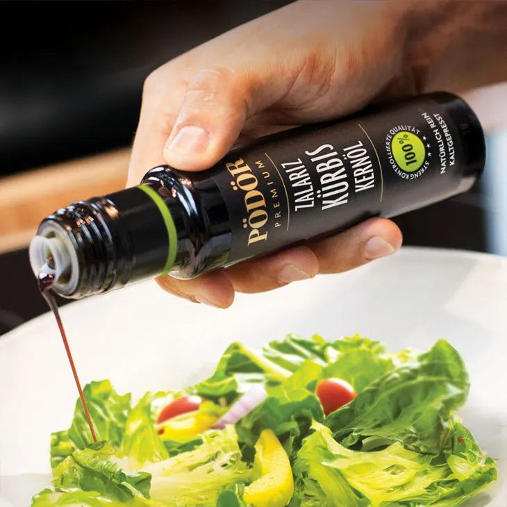 Pödör Zalariz Kürbiskernöl wird aus der dunklen Glasflasche über einen frischen Blattsalat gegossen.