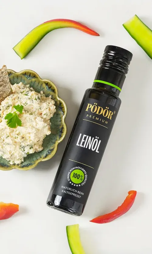 Flasche Pödör Leinöl auf hellem Untergrund, daneben eine Schale Kräuterquark mit Paprika- und Gurkenstücken.