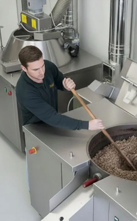 Mitarbeiter rührt in der Ölmühle die erwärmte Kürbiskernmasse in einem großen Kessel, bevor sie in die Stempelpresse kommt.